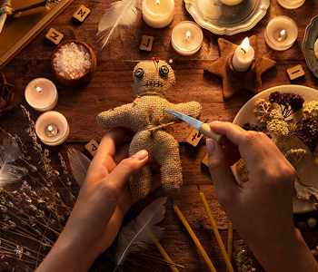 Hands preparing a ritual doll surrounded by candles, dried herbs and runes