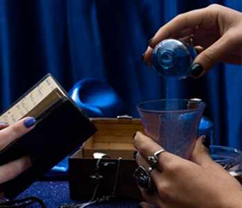 Hands pouring blessed water from a blue vial into a glass
